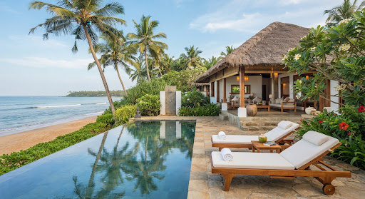 A serene private boutique beach villa in Bentota Sri Lanka with sun loungers beside a reflective pool overlooking calm ocean waves, flanked by tall sw